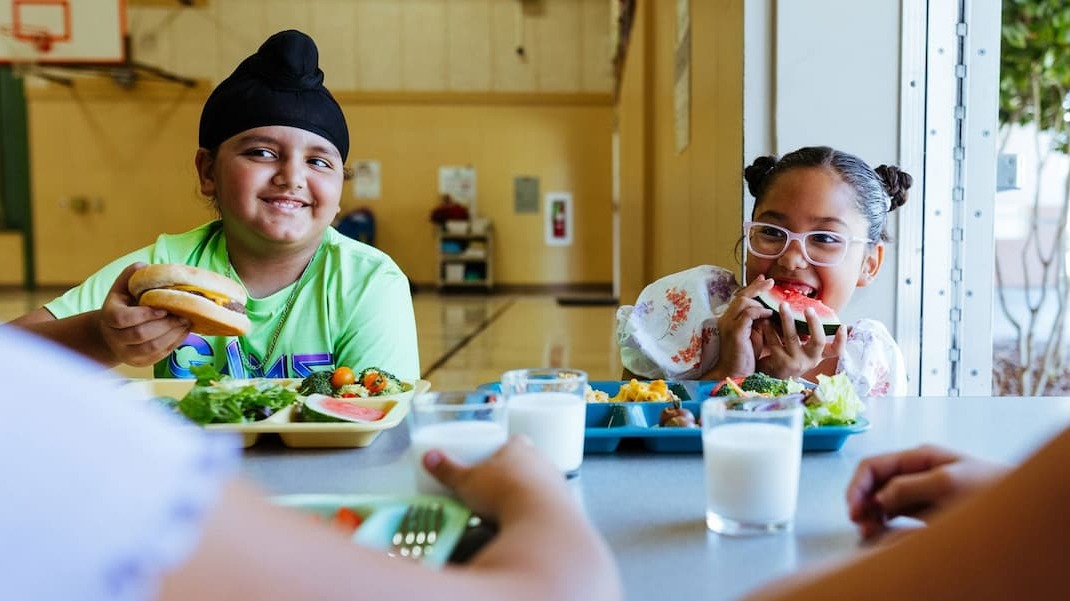 Two kids eating lunch in a cafeteria.