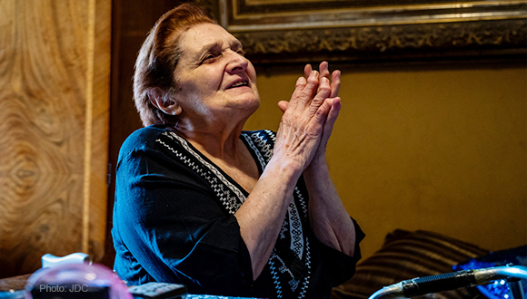 An elderly woman with her hands folded in prayer.