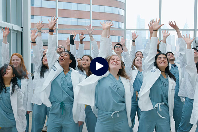 Penn Medicine students in scrubs holding their hands up to the sky.