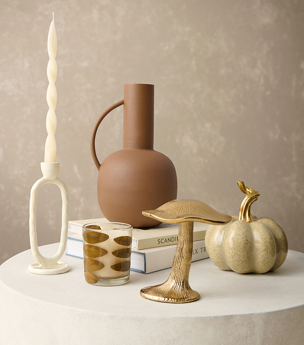 Neutral home decor including a vase, candle holder, books, mushroom ornament, candle and pumpkin.