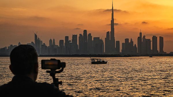 A man stands holding a smartphone in front of the Dubai skyline, with the Burj Khalifa, the world's tallest building, seen from Creek Harbour, UAE.