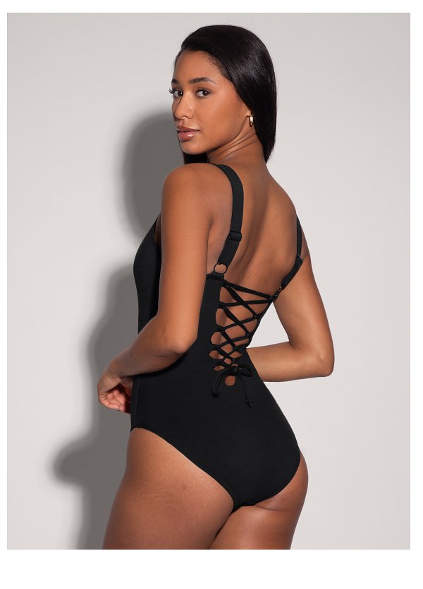 A woman in a black swimsuit with a lace-up back, posing sideways against a light background.