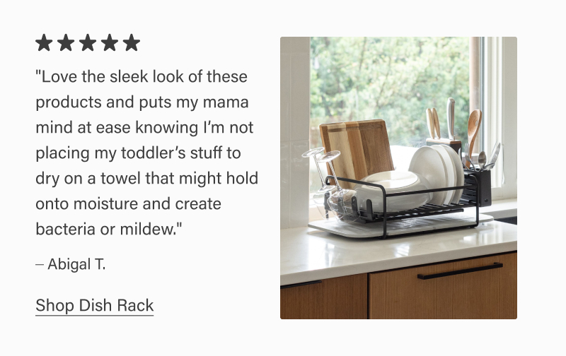 Dorai dish rack holding plates, glasses, and utensils on a kitchen counter by a window. Five-star review reads: “Love the sleek look… not placing my toddler’s stuff on a towel that might hold moisture and create bacteria or mildew.” – Abigail T. Text link: “Shop Dish Rack.”