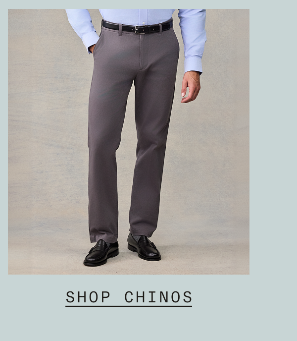 Man wearing gray chinos with a light blue dress shirt and black belt, paired with black penny loafers. Text: "SHOP CHINOS"