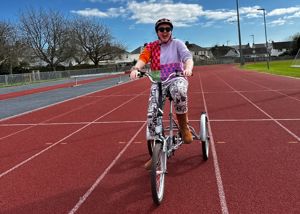 A rider in bright patterned clothing rides a tricycle on a dark red athletics track.
