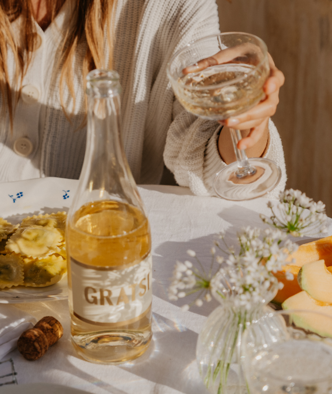 Woman holding a wine glass of Gratsi Sparkling White Wine while sitting at a table set with food and flowers