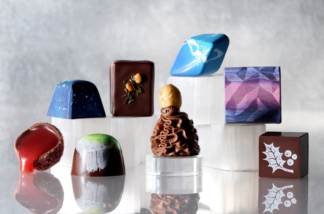 Individual confections in varying shapes and sizes. Some are painted shades of blue or purple. One is sliced in half and has caramel pouring out. 