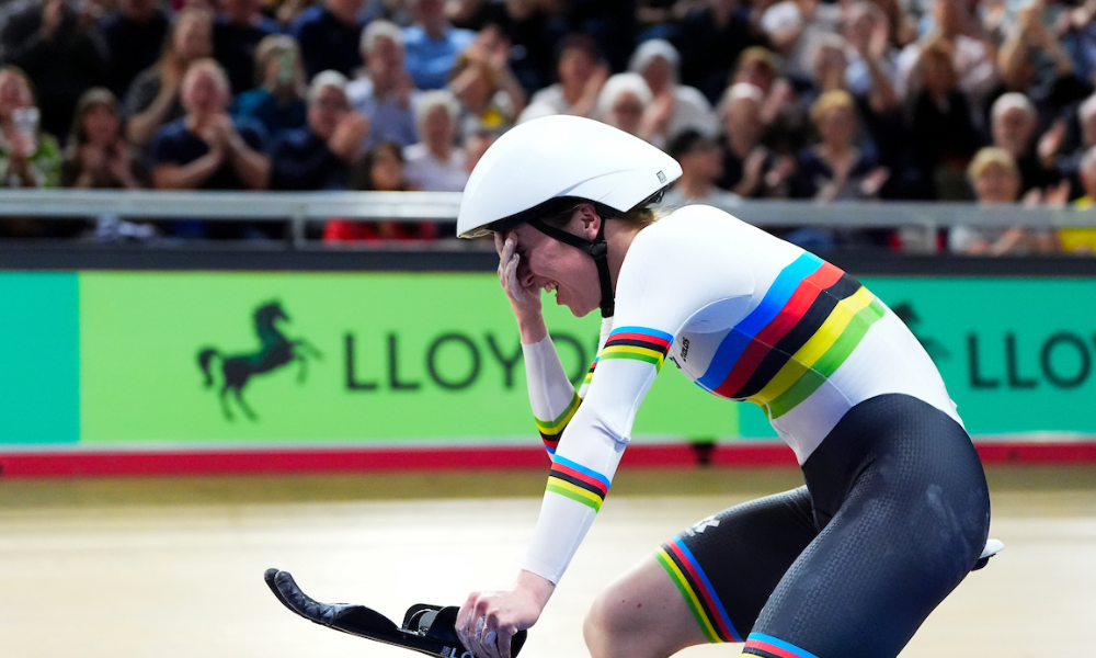 Anna holds her hand to her face in disbelief after winning an event on the track, with the crowd blurred in the background.