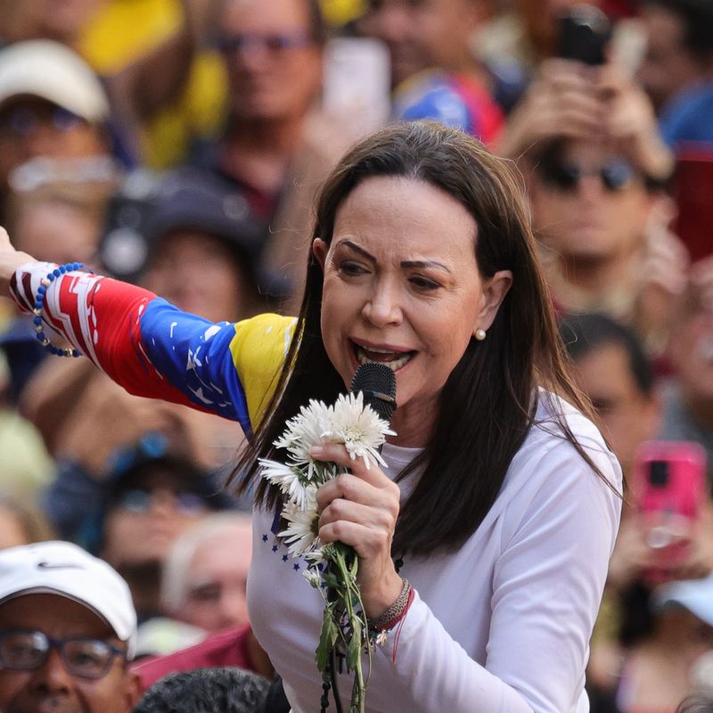 A woman holding a microphone speaks in front of a crowd.
