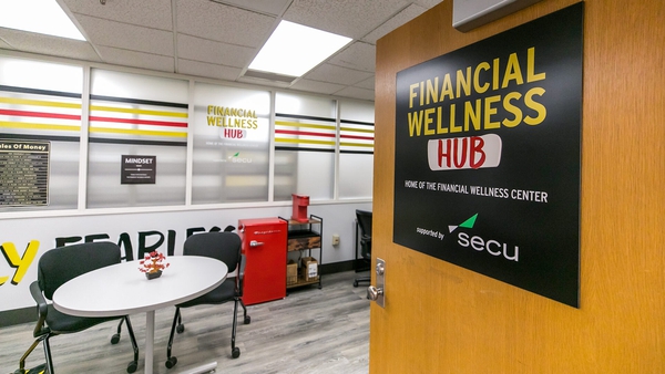 Picture of room that houses Financial Wellness Hub, including tables, chairs and other furniture with a sign with the name on door.