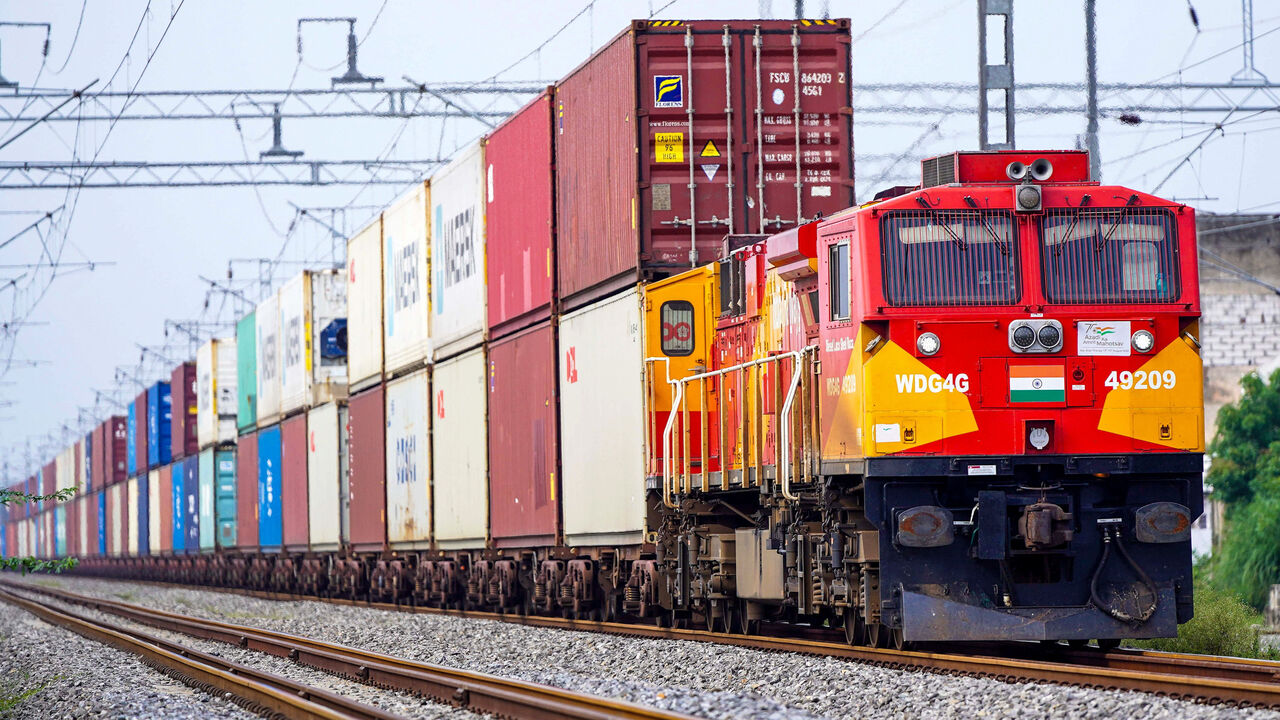 A freight train with an Indian flag on the front carrying cargo containers rides along a railway track in Ajmer, India.