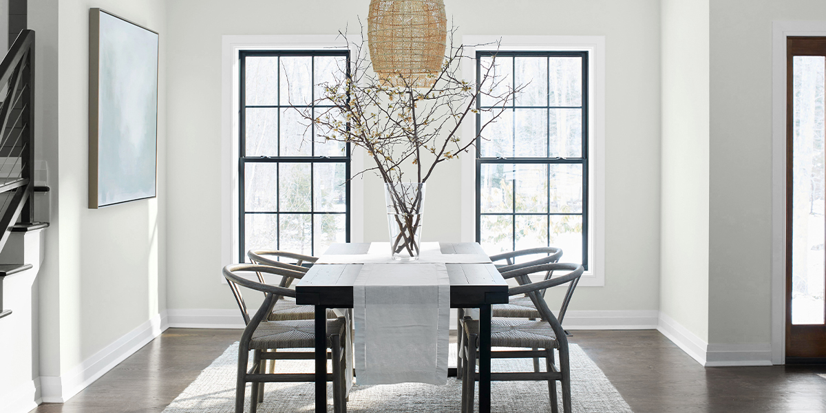A serene dining room with off-white-painted walls, a light-gray ceiling and trim, black wood table and chairs, and wicker chandelier.