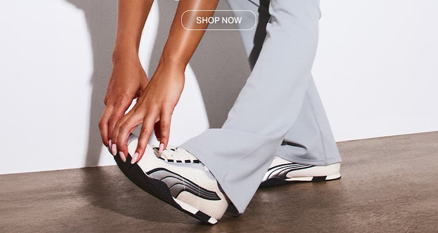 Person in light blue activewear pants bending to touch stylish beige and black trainers. Shop now for trendy women's athletic shoes.