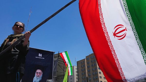 A woman waves an Iranian flag in front of a poster of the Supreme Leader Ayotollah Ali Khemenei in Tehran