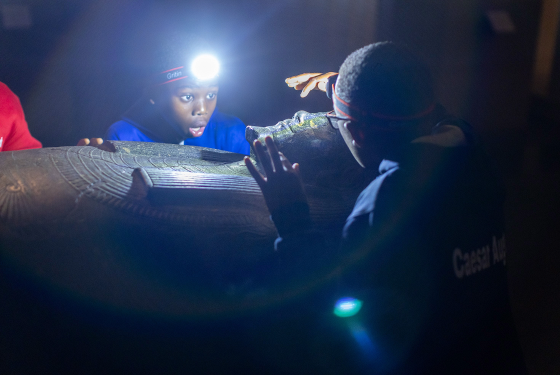 Children with head torches looking at Egyptian sculptures.