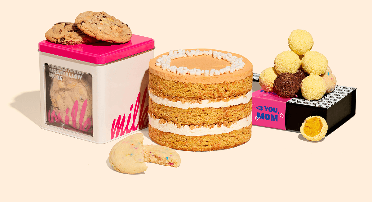 GIF cycling through bundled desserts on a cream background — a carrot layer cake with white frosting and marshmallow topping, assorted cake truffles on a black box with a pink sleeve that reads “<3 YOU, MOM,” a cookie tin with “Milk Bar” branding and cookies on top, and stacked Milk Bar Pie slices.