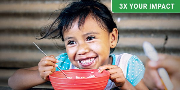 A girl with rice grains on her mouth smiles over a bowl of Vitafood. 