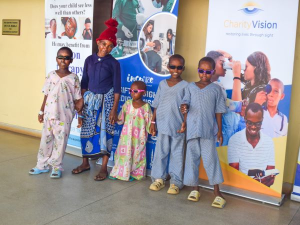 Alt-text: Elizabeth, a mother in Kenya, stands with her four children after surgery
