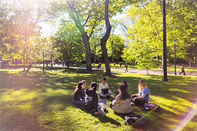 A group of people sitting on the grass of College Green.
