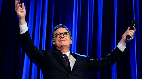 Stephen Colbert stands with his arms outstretched.