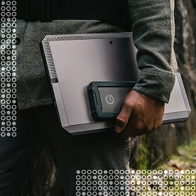A person holding a laptop and an external hard drive outdoors, with a pattern of white and yellow circles overlaying the image.