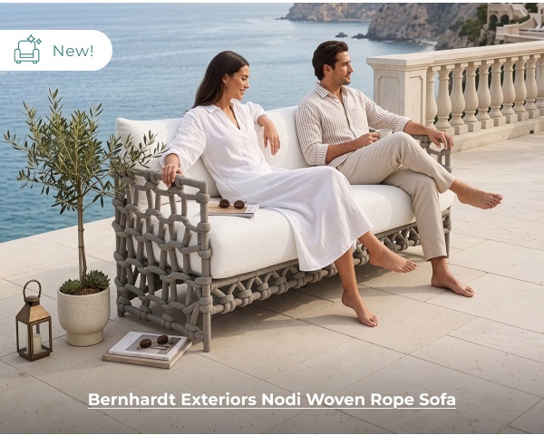 A man and a woman lounge together on a modern outdoor sofa featuring a distinct grey thick-woven rope frame on a coastal stone patio. Image Text: New! Bernhardt Exteriors Nodi Woven Rope Sofa