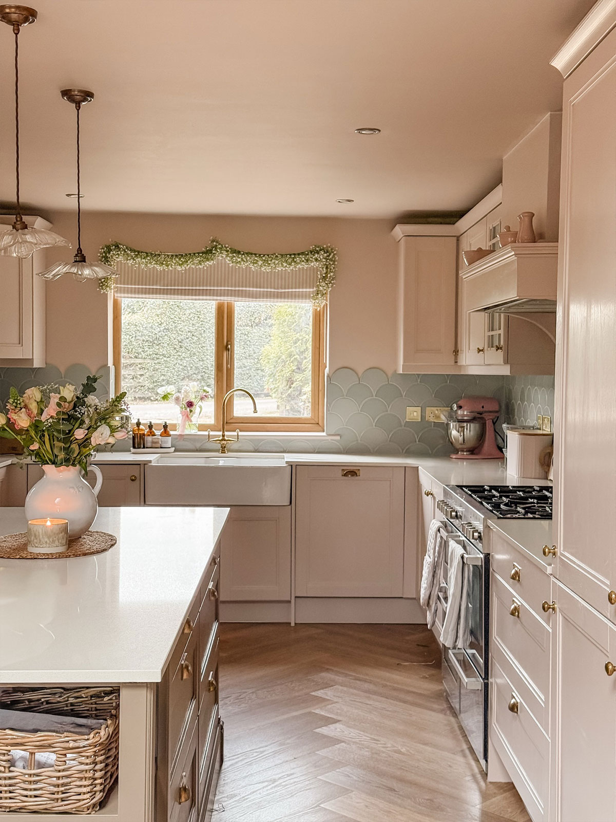 This kitchen is soft and romantic, with its pastel pink walls and units contrasting with pale-grey scalloped edge tiles, like pretty fish scales around the space. A swag of white flowers sits on top of the pink and white striped window blind, emphasising the softness of the space. The overall effect is one of calmness, showing peaceful retreats can be created in any colour with the right shade combinations.