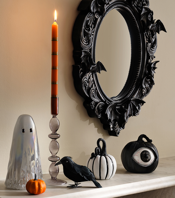 Black bat mirror with Halloween decor, including a candle, ceramic ghost, black crow and pumpkin ornaments.