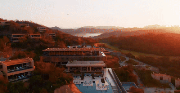 Hero video featuring 4 scenes: 1) Aerial view of the resort at sunset 2) A couple running along the beach 3) A group of people diving off a fishing boat. 4) A group of people dining al fresco.