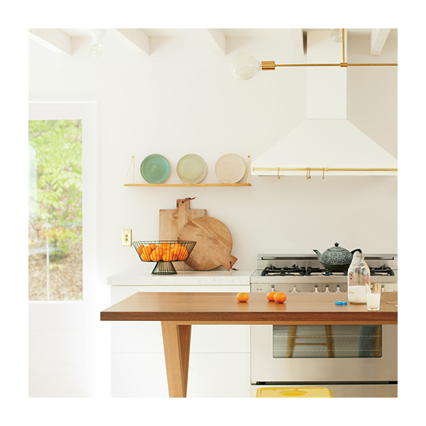A close up of a white kitchen with a white range hood above a stove with open shelves on either side with colored plates on display.