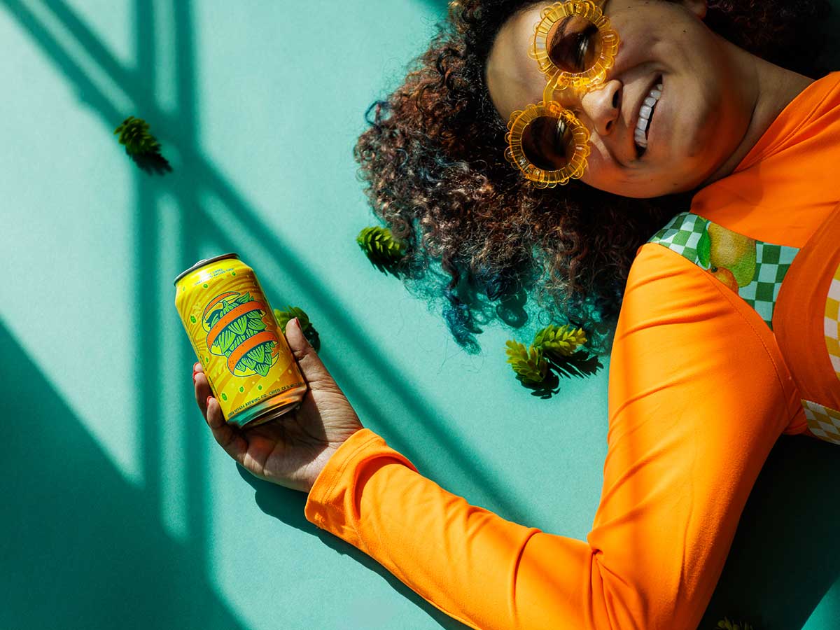 A smiling woman lying on the ground and holding a can of Citra Little Thing