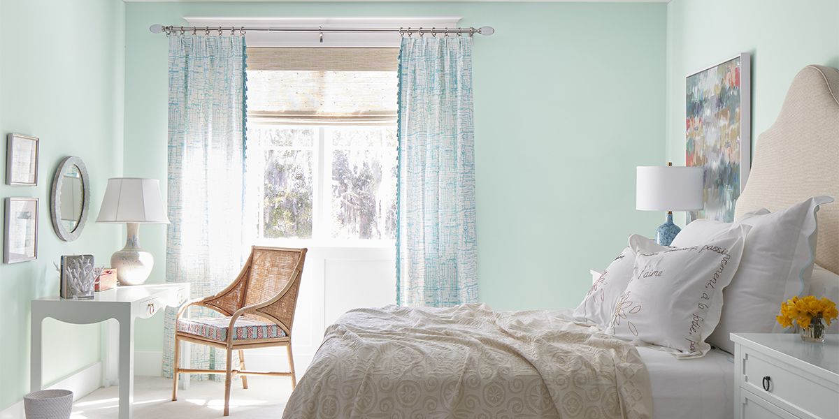 A beachy bedroom painted in a minty green hue with white ceiling, white-painted dresser, and off-white carpeting. 