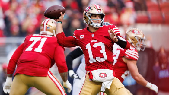 A player in 49ers uniform holds a ball aloft.