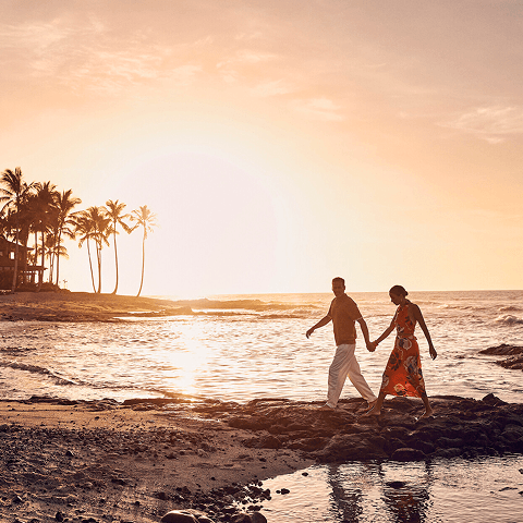 A couple walking along a black lava stone coastline at sunset.