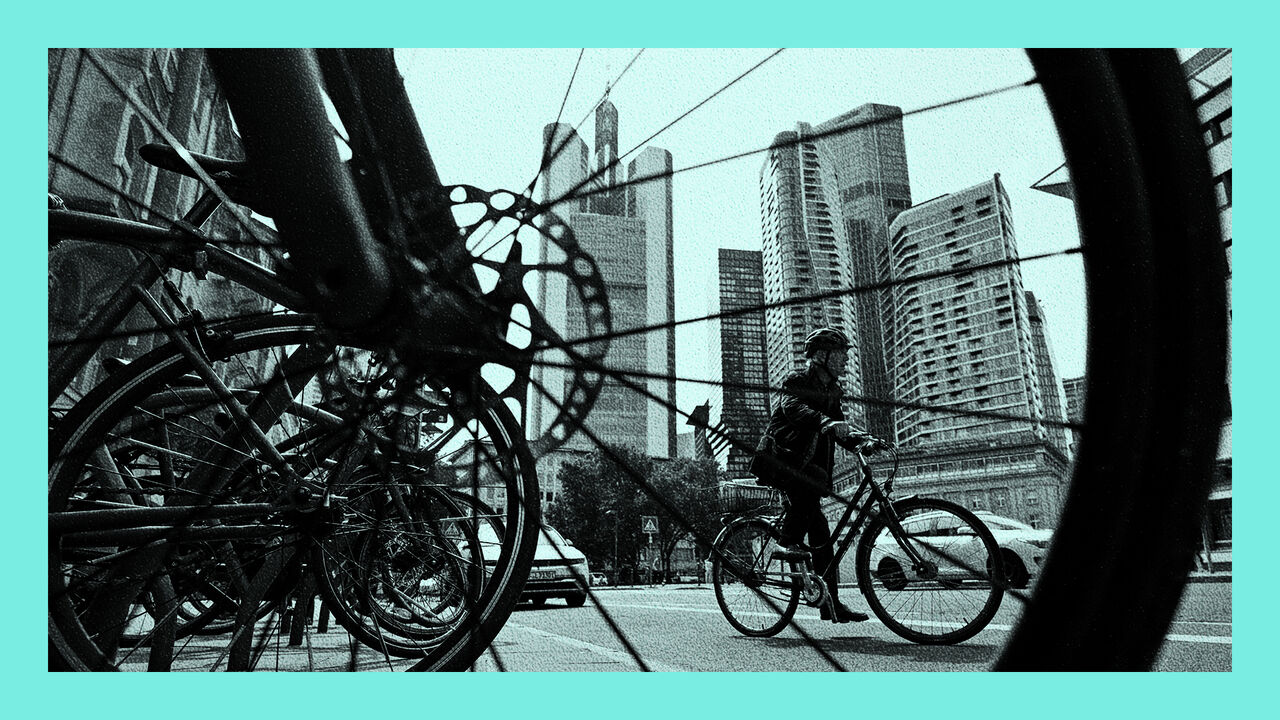 The view throgh a bicycle wheel, a person rides a bicycle in front of the banking district skyline with the Commerzbank building in Frankfurt am Main, western Germany.