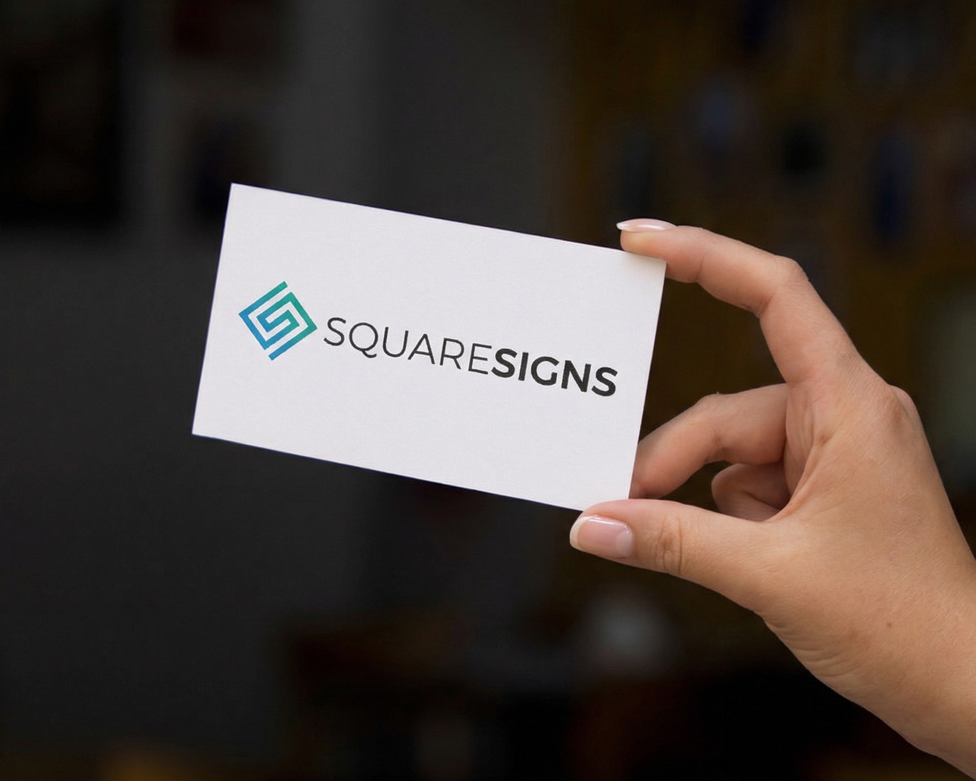 Hand holding a white business card with the SquareSigns logo and name printed in teal and black.
