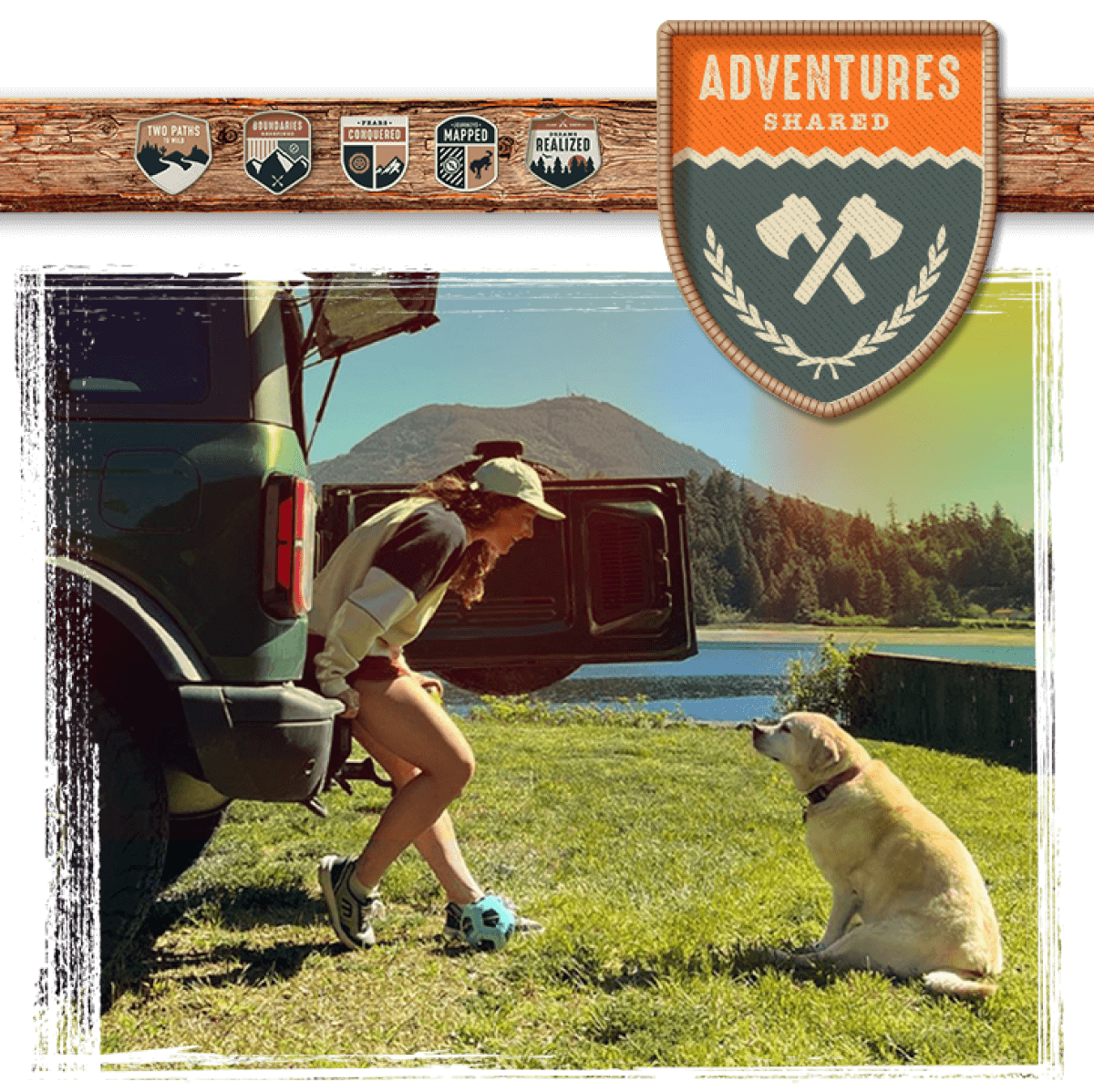 A woman sitting on the rear bumper of a Bronco&reg; SUV, smiling at a dog seated on the ground in front of her
