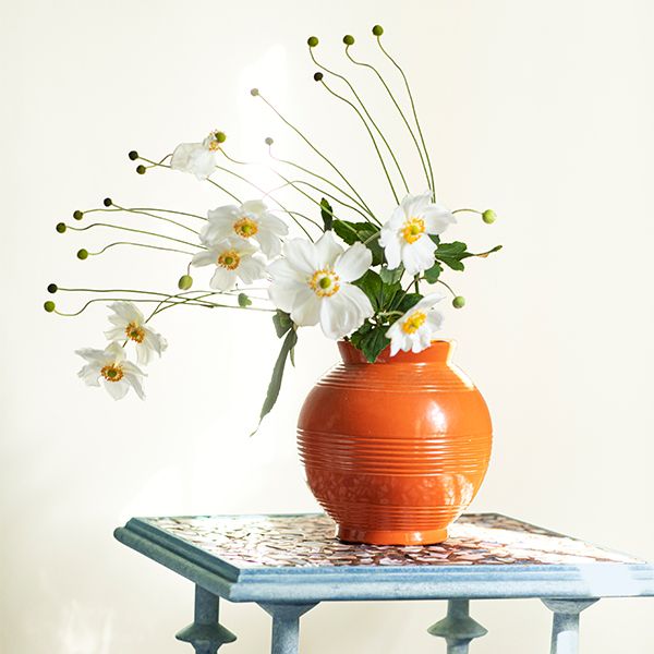 A blue table with a vase full of white flowers against an off-white-painted wall.