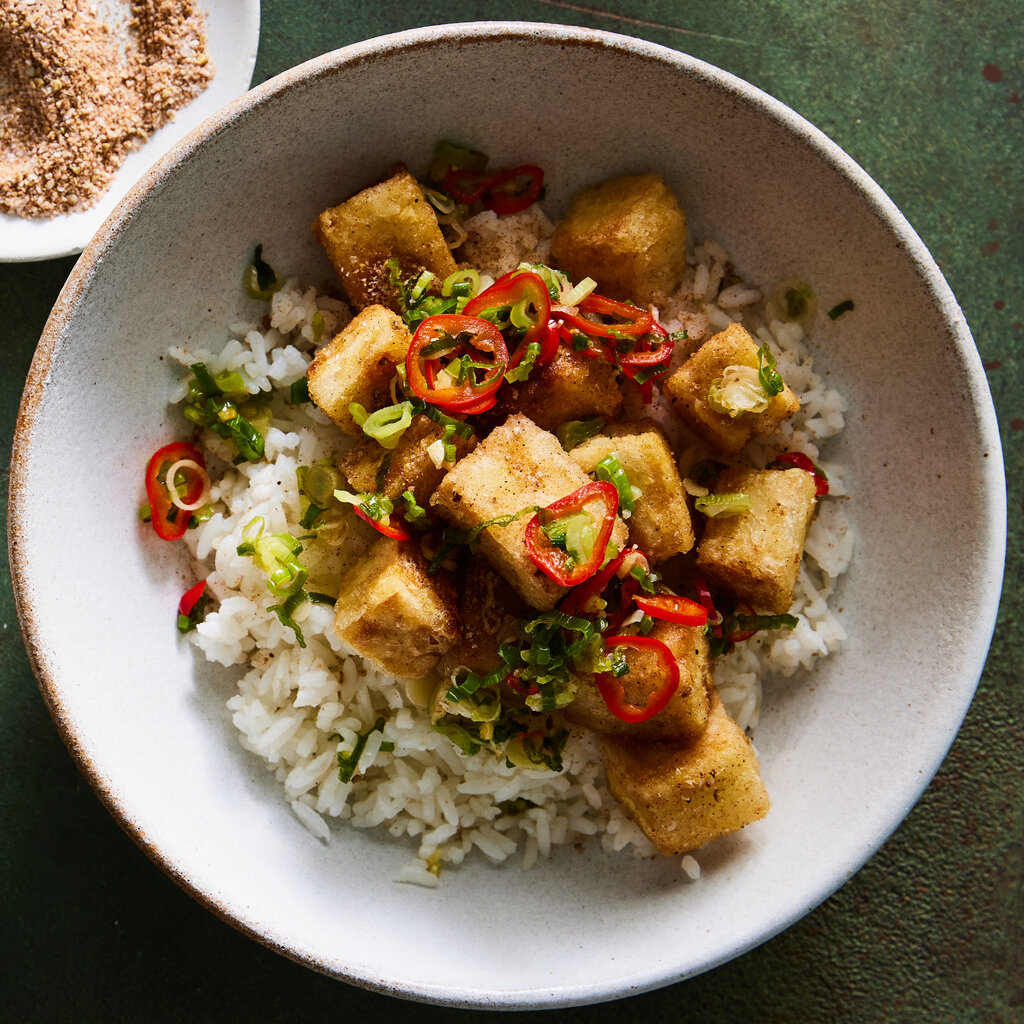Cubes of salt and pepper tofu over rice in a white bowl.