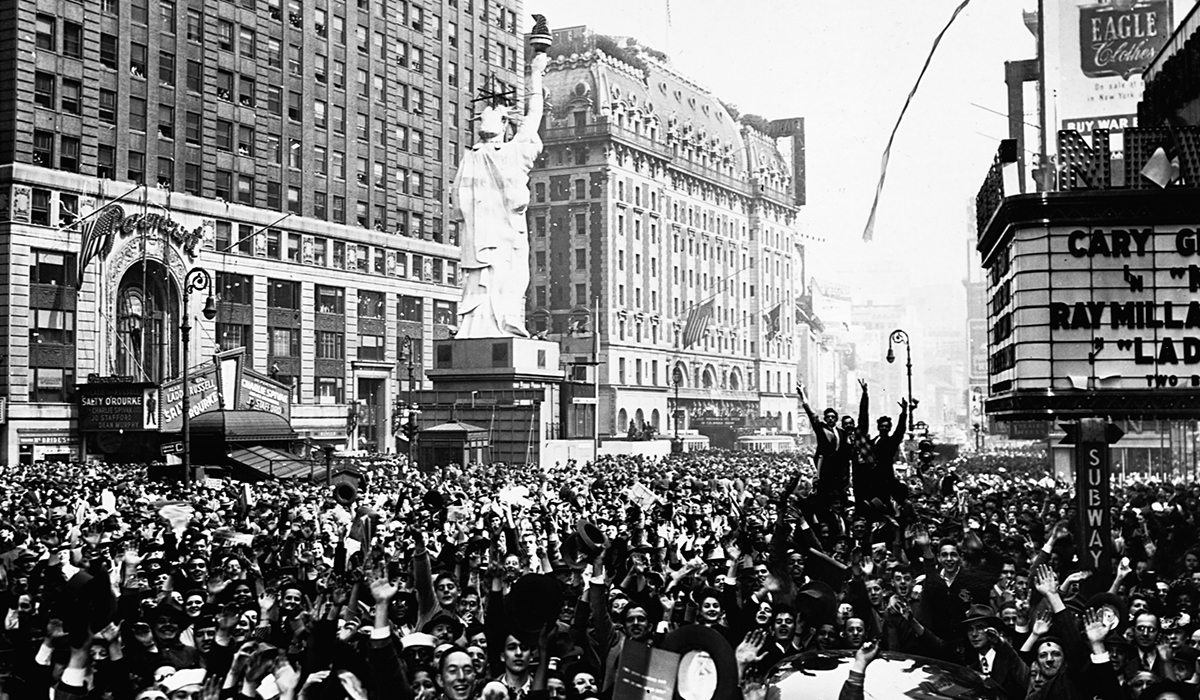 A huge crowd of people fill a street in celebration.