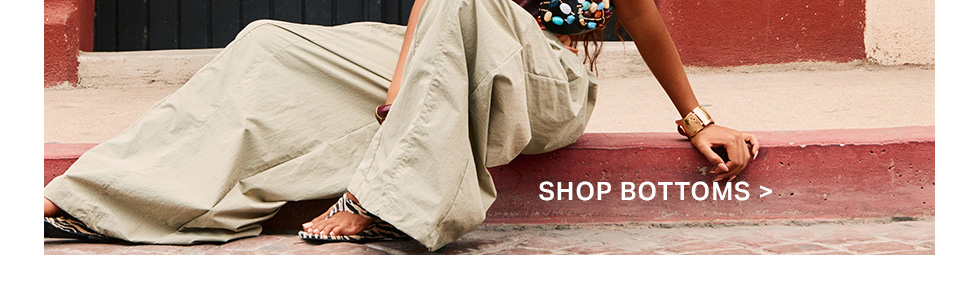 Person in wide-leg khaki pants and zebra sandals sits on a red curb. Shop our comfortable women's bottoms collection.