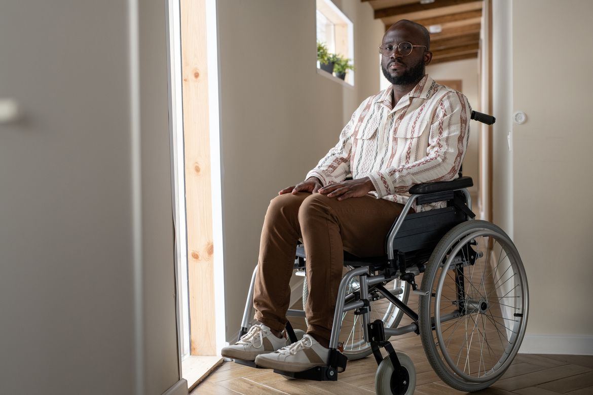 Young Black man faces camera while sitting on wheelchair in corridor of apartment