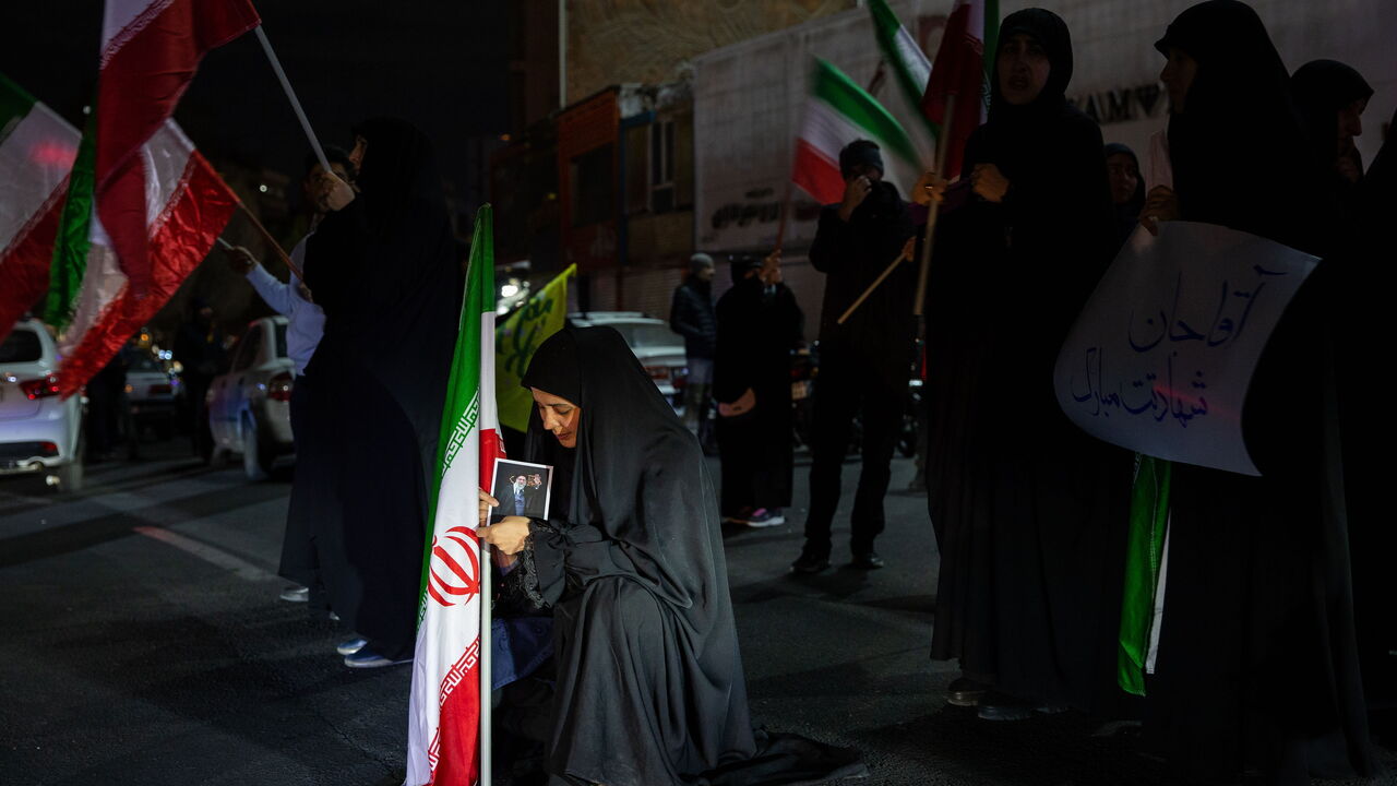 A woman sitting holding an Iranian flag at a vigil after the supreme leader, Ayatollah Khamenei was killed by US-Israel airstrikes in Tehran.