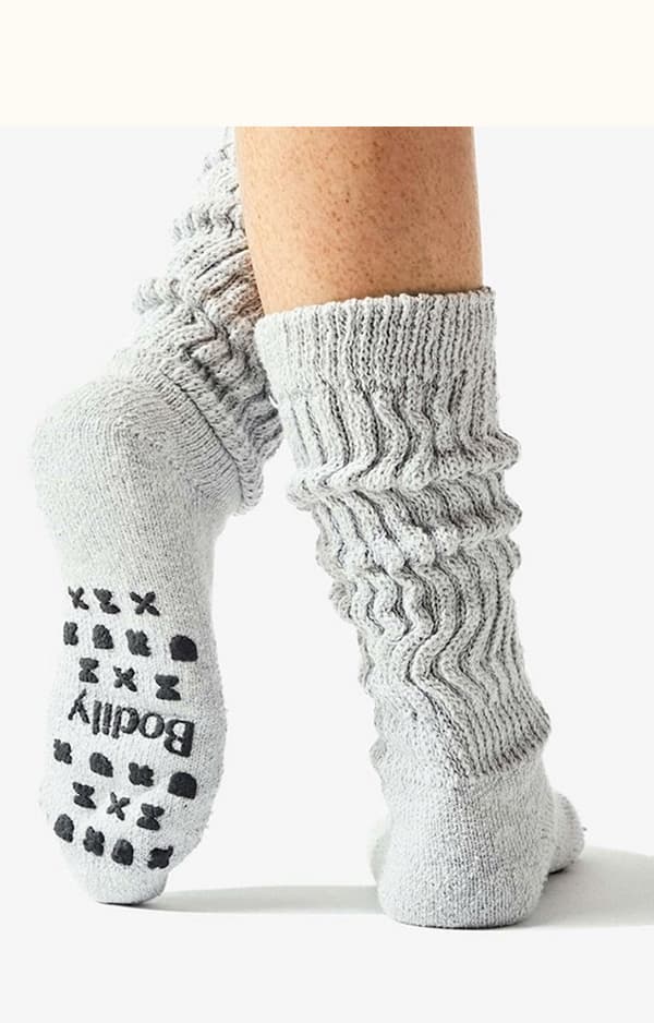 A picture of someone wearing grey cozy socks with black silicone grips on the bottom. 