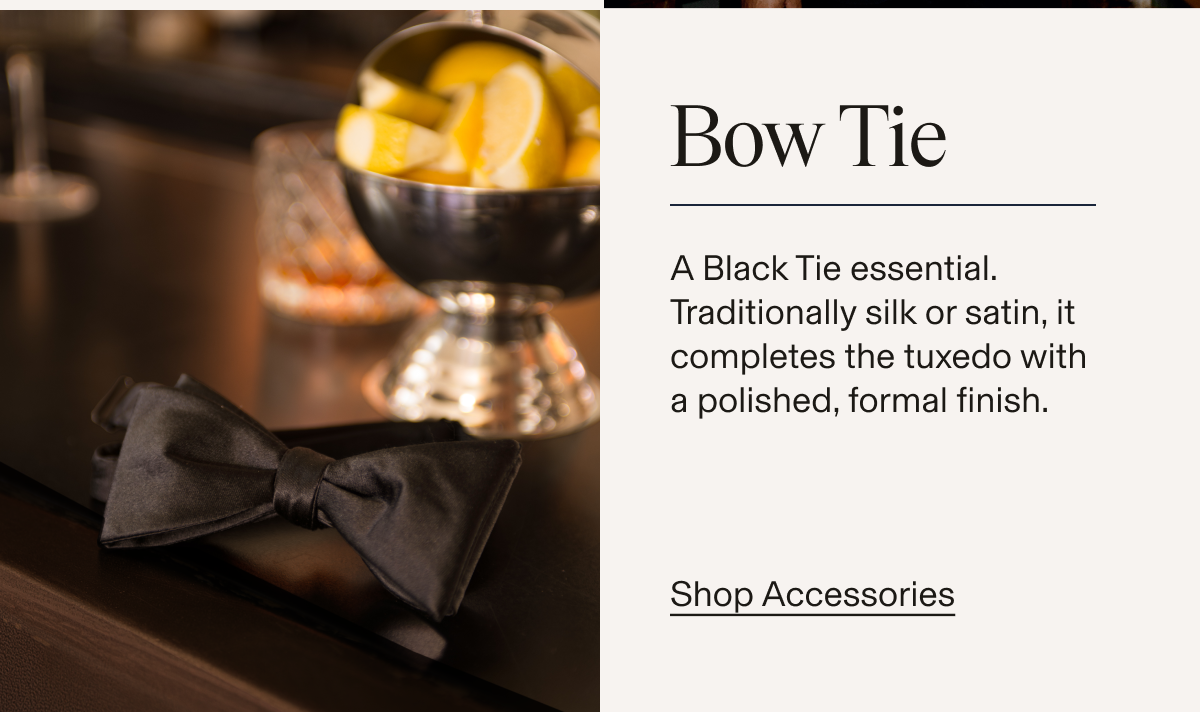 A black satin bow tie resting on a dark surface in front of a silver cocktail shaker and a bowl of lemon wedges. Text reads: "Bow Tie. A Black Tie essential. Traditionally silk or satin, it completes the tuxedo with a polished, formal finish. Shop Accessories"