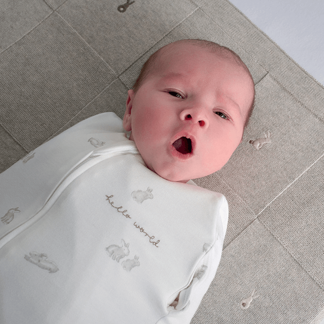 Baby yawning in bunny style swaddle, lay on bunny embroidered blanket