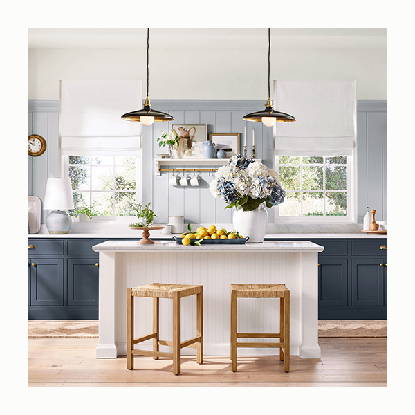 A luxurious open kitchen with navy cabinetry, a white shiplap kitchen island, rattan and wood barstools, and overhead pendant lighting.