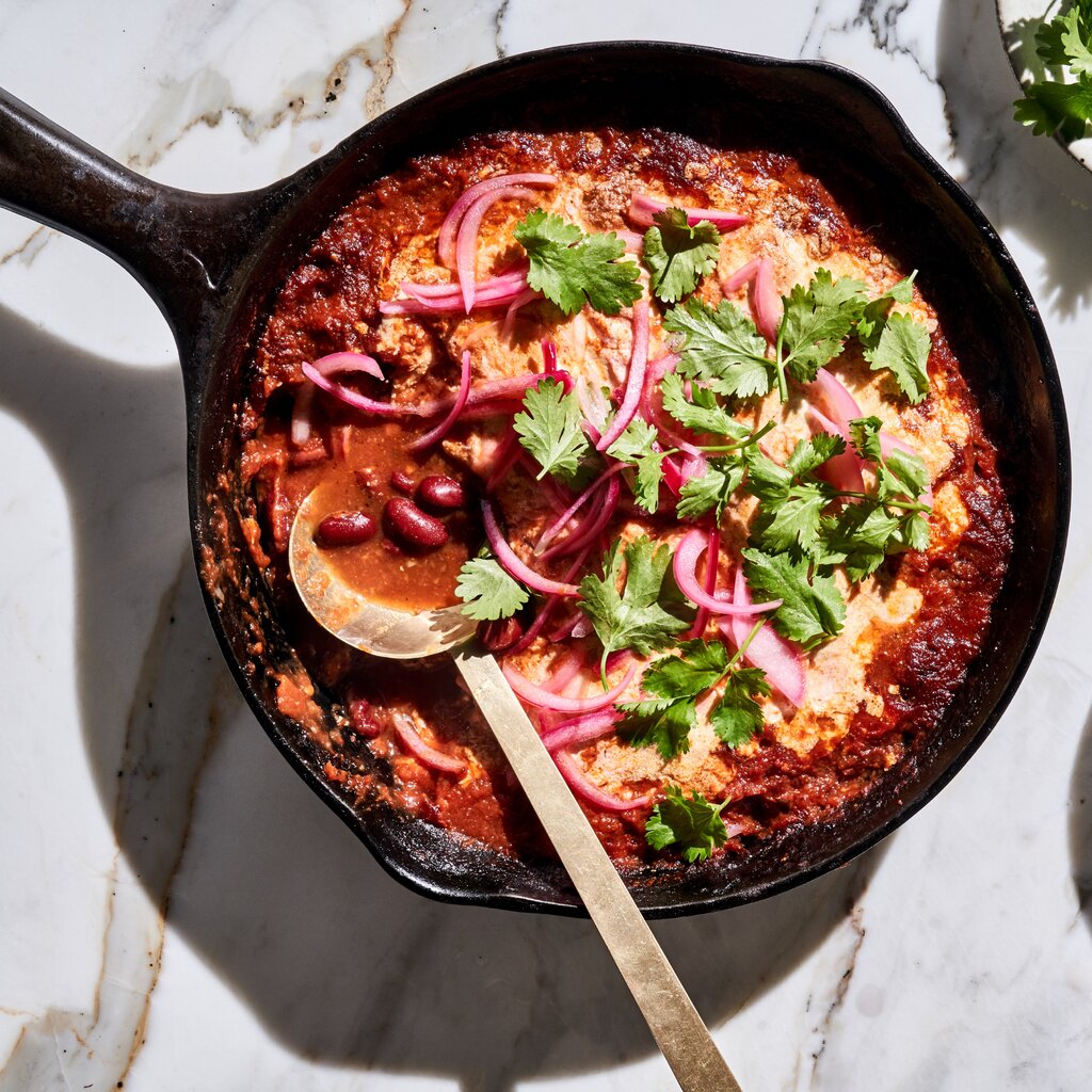 Red bean stew topped with cheese, pickled onions and parsley in a cast-iron skillet.