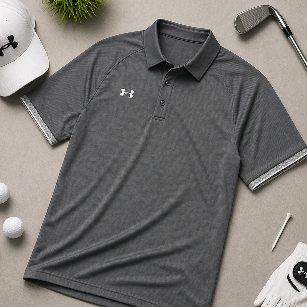 Gray Under Armour polo shirt laid flat with golf accessories including cap, clubs, balls, and glove on beige background.