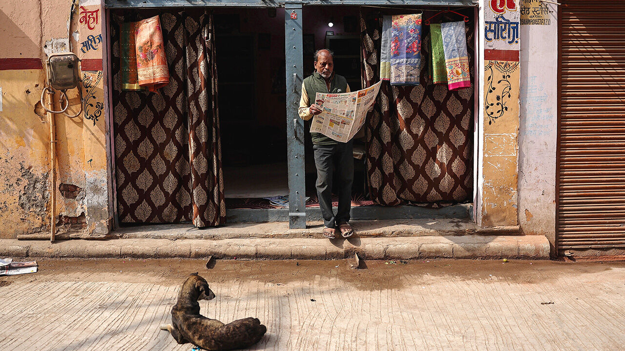 A saree vendor reads a newspaper outside his shop in Varanasi on January 29, 2026. 